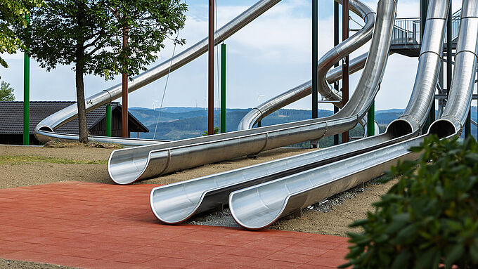 Several stainless steel slides end on a red surface made of REGUPOL playfix FX50 safety tiles at Panorama Park Sauerland