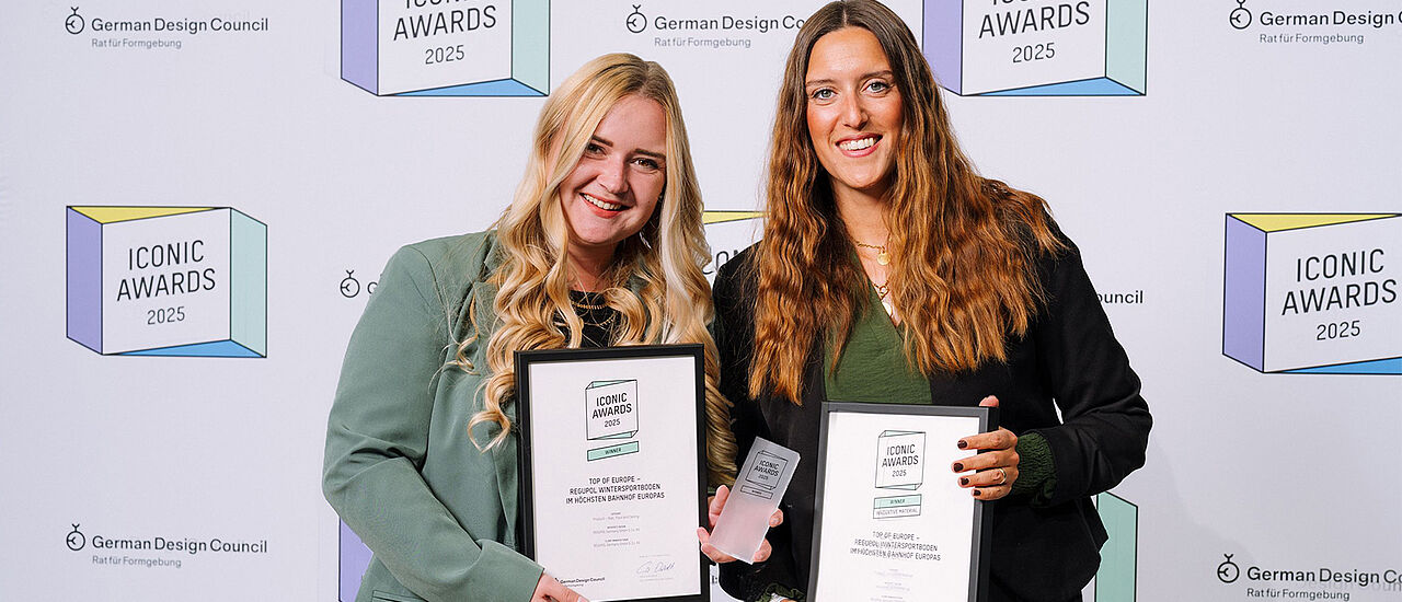 Two women are each holding a certificate in a black frame. 